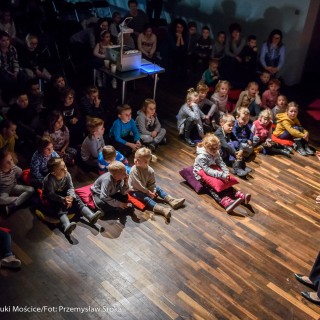 "Pan Dźwięk" - spektakl i warsztaty - Dzieci siedzą na podłodze, patrzą na aktorkę. Aktorka wykonuje gesty rękami.