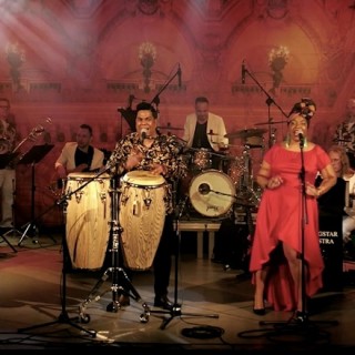 Muzyczne Tarasy - One Night in Havana Salsa Latina - Zesp&oacute;ł na scenie. Kobieta w czerwonej sukni, mężczyzna z bębnami.
