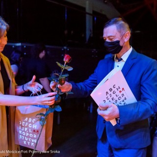 Małopolska Nagroda Poetycka ŹRÓDŁO edycja czwarta - Kobieta wręcza mężczyźnie róże oraz trzyma w drugiej ręce torbę papierową. Mężczyzna trzyma w ręce teczkę i odbiera róże.  - Fot: Przemysław Sroka