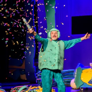 "Wystarczy być" - spektakl dla dzieci Teatru Maska - Mężczyzna w zielonym przebraniu wystrzela kolorowe confetti. - Fot : Przemysław Sroka