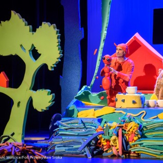 "Wystarczy być" - spektakl dla dzieci Teatru Maska - Na scenie mężczyzna przebrany na czerwono trzyma w rękach dużą, sztuczną mrówkę. Obok kobieta w przebraniu. - Fot : Przemysław Sroka