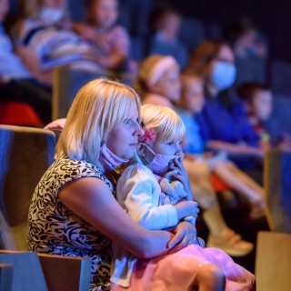 "Wystarczy być" - spektakl dla dzieci Teatru Maska - Kobieta z dzieckiem siedzi na widowni i ogląda przedstawienie. W tle reszta publiczności - Fot : Przemysław Sroka