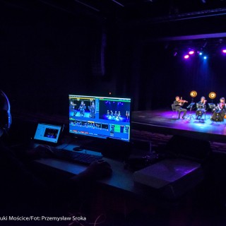 Koncert Patriotyczny Kwartetu Smyczkowego Filharmonii Krakowskiej - Na komputerze wyświetla się nagranie występu. W tle, na scenie, trwa występ.