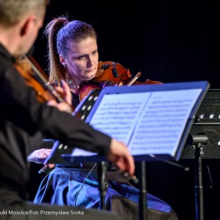 Koncert Patriotyczny Kwartetu Smyczkowego Filharmonii Krakowskiej - Mężczyzna i kobieta grają na skrzypcach patrząc na nuty.