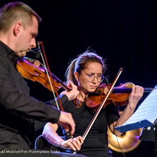 Koncert Patriotyczny Kwartetu Smyczkowego Filharmonii Krakowskiej - Mężczyzna i kobieta grają na skrzypcach patrząc na nuty.