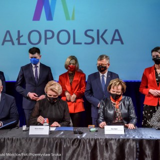 Podpisanie porozumienie na rzecz rozwijania i promowania kultury - Grupa kobiet i mężczyzn stoi za stołem, przy którym siedzą cztery osoby z długopisami w dłoni. - Fot: Przemysław Sroka