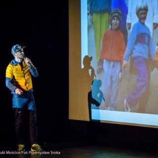Festiwal Górnolotni 2021. Dzień pierwszy. - Mężczyzna w czapce mówi do mikrofonu spoglądając na ekran, na którym wyświetla się zdjęcie trójki dzieci. - Fot : Przemysław Sroka
