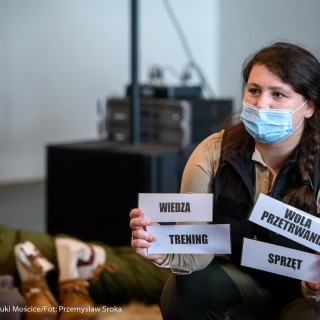 Festiwal Górnolotni 2021. Dzień pierwszy. -  Kobieta w maseczce pokazuje kartki z napisami: ,,wiedza" ,,wola przetrwania" ,,trening" ,,sprzęt" - Fot : Przemysław Sroka
