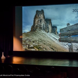 Festiwal Górnolotni 2021. Dzień pierwszy. - Mężczyzna w lewym dolnym rogu mówi do mikrofonu spoglądając na ekran, na którym wyświetla się zdjęcie gór i drogowskazów. - Fot : Przemysław Sroka