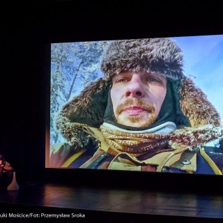 Festiwal Górnolotni 2021. Dzień pierwszy. - Kobieta i mężczyzna w lewym dolnym rogu wpatrują się w ekran, na którym wyświetlone jest zdjęcie mężczyzny w futrzanej czapce i zimowy krajobraz. - Fot : Przemysław Sroka