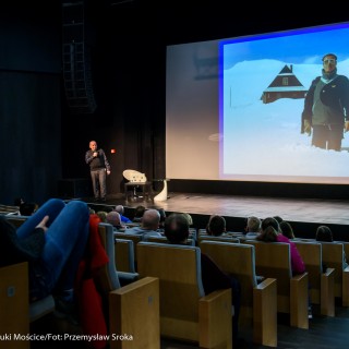 Festiwal Górnolotni 2021. Dzień drugi. - Ludzie w maseczkach siedzą na widowni i spoglądają w stronę ekranu, na którym wyświetla się zdjęcie dwóch mężczyzn w śniegu. - Fot : Przemysław Sroka