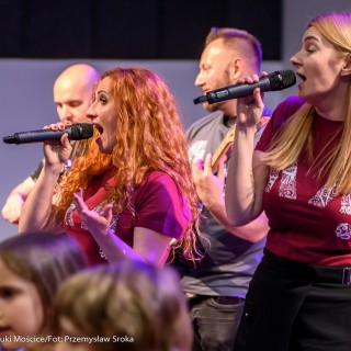 Akcja muzyczna na 50-lecie Centrum - Dwie kobiety w bordowych koszulkach śpiewają do mikrofonów, za nimi dwóch mężczyzn gra na gitarach.  - Fot. : Przemysław Sroka
