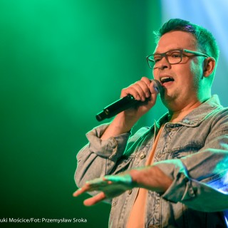 "Znów wędrujemy" - widowisko muzyczne - Mężczyzna w okularach śpiewa do mikrofonu.  - Fot. : Przemysław Sroka