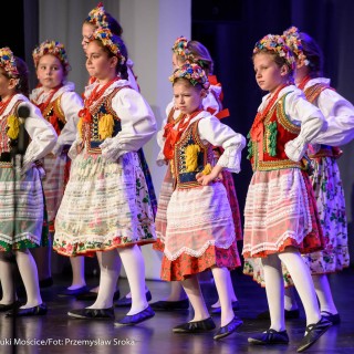 "Matulu, wyjrzyj na próg chaty" - występ Małych Świerczkowiaków - Grupa dziewczynek w kolorowych strojach ludowych tańczy na scenie z rękami założonymi na biodrach. - Fot. : Przemysław Sroka