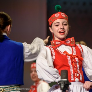 "Matulu, wyjrzyj na próg chaty" - występ Małych Świerczkowiaków - Kobieta w czerwonym stroju ludowym śpiewa, za nią stoi odwrócony mężczyzna w niebieskim stroju ludowym. - Fot. : Przemysław Sroka