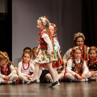 "Matulu, wyjrzyj na próg chaty" - występ Małych Świerczkowiaków - Dziewczynki w kolorowych strojach ludowych z wiankami na głowach siedzą na podłodze, dwie z nich tańczą na środku na scenie. - Fot. : Przemysław Sroka