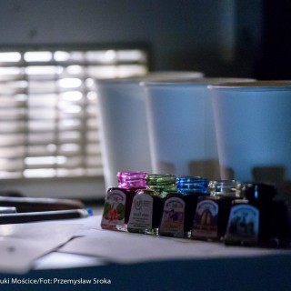 "Pan Dźwięk" - spektakl i warsztaty - Na stoliku stoją trzy papierowe kubki, przed nimi ustawionych jest pięć małych pojemników z barwnikami o różnych kolorach.  - Fot. : Przemysław Sroka