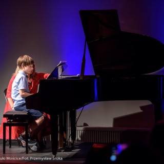 MiniLab - zakończenie roku 2020/2021 - Kobieta w czerwonej sukience pokazuje nuty chłopczykowi, który siedzi przy fortepianie.  - Fot. :Przemysław Sroka