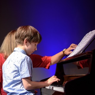 MiniLab - zakończenie roku 2020/2021 - Kobieta w czerwonej sukience pokazuje nuty, a chłopczyk gra na fortepianie.   - Fot. :Przemysław Sroka