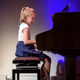 MiniLab - zakończenie roku 2020/2021 - Dziewczynka w białej bluzce i granatowej spódnicy gra na fortepianie.  - Fot. :Przemysław Sroka