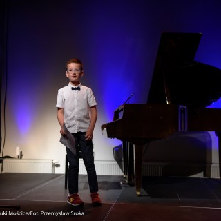 MiniLab - zakończenie roku 2020/2021 - Chłopczyk w okularach i koszuli stoi na scenie obok fortepianu i trzyma kartkę z nutami w ręce.  - Fot. :Przemysław Sroka