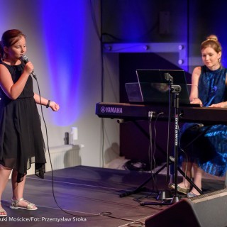 MiniLab - zakończenie roku 2020/2021 - Dziewczynka w czarnej sukience śpiewa do mikrofonu na scenie, a kobieta w niebieskiej sukience gra na keyboardzie.  - Fot. :Przemysław Sroka