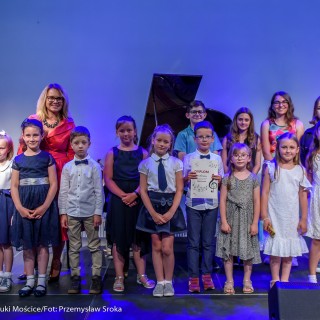 MiniLab - zakończenie roku 2020/2021 - Na scenie w rzędzie stoi grupa dzieci, dwoje z nich pokazuje dyplom, za nimi stoją kobiety w czerwonej i niebieskiej sukni.  - Fot. :Przemysław Sroka