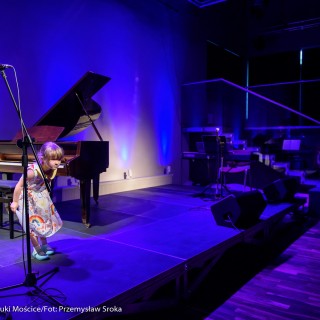 MiniLab - zakończenie roku 2020/2021 - Dziewczynka w kolorowej sukience stoi na scenie obok fortepianu i kłania się widowni.  - Fot. :Przemysław Sroka