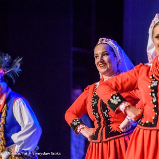 Świerczkowiacy - zakończenie sezonu artystycznego 2020/2021 - Dwie kobiety w czerwonych strojach ludowych tańczą na scenie, za nimi mężczyzna w niebieskim stroju ludowym. - Fot. :Przemysław Sroka