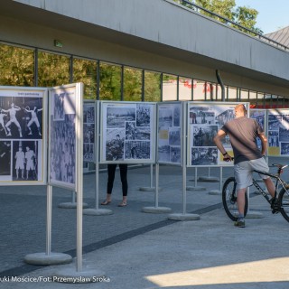 Mościce mam w sercu - wystawa - Stojaki z wystawą zdjęć ustawione na zewnątrz, mężczyzna na rowerze i kobieta, oglądają je. - Fot. :Przemysław Sroka