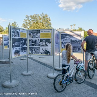 Mościce mam w sercu - wystawa - Stojaki z wystawą zdjęć ustawione na zewnątrz, mężczyzna oraz dziewczynka na rowerach oglądają je. - Fot. :Przemysław Sroka