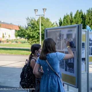 Mościce mam w sercu - wystawa - Kobieta w niebieskiej sukience oraz dziewczynka oglądają wystawę zdjęć ustawioną na zewnątrz. - Fot. :Przemysław Sroka