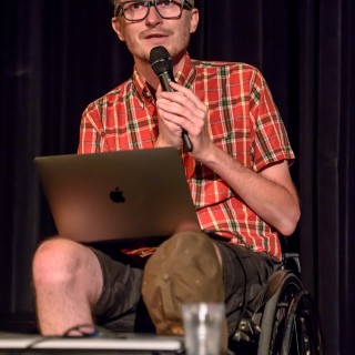 Festiwal Dalekosiężni 2021. Dzień pierwszy. - Mężczyzna na wózku inwalidzkim z laptopem mówi do mikrofonu. - Fot. :Przemysław Sroka