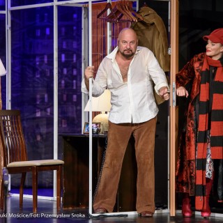 "Bożyszcze kobiet" - spektakl Teatru Capitol - Kobieta i mężczyzna stoją po dwóch stronach drzwi dotykając klamki. Mężczyzna ma rozpiętą  koszulę, kobieta ubrana jest w czapkę i szalik. - Fot.: Przemysław Sroka