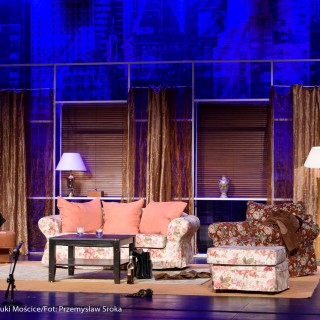 "Bożyszcze kobiet" - spektakl Teatru Capitol - Kobieta i mężczyzna siedzą po dwóch stronach sceny. Kobieta mówi coś gestykulując, mężczyzna siedzi na krześle i dotyka swojej stopy. - Fot.: Przemysław Sroka