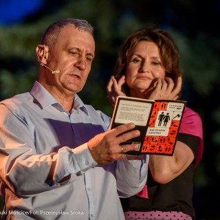 "Małe zbrodnie małżeńskie" - Muzyczne Tarasy 2021 - Kobieta w czarnej bluzce i różowej chustce oraz mężczyzna w koszuli patrzą na książkę o tytule 'Małe zbrodnie małżeńskie.' - Fot.: Przemysław Sroka