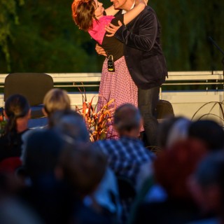 "Małe zbrodnie małżeńskie" - Muzyczne Tarasy 2021 - Kobieta w czarnej bluzce i różowej chustce stoi przytulona z mężczyzną w marynarce, oboje uśmiechają się do siebie. - Fot.: Przemysław Sroka