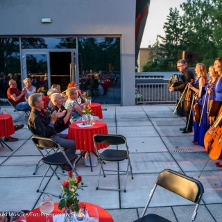 Con Affetto i Klaudiusz Baran - Muzyczne Tarasy 2021 - Ludzie na widowni klaszczą. Siedzą przy okrągłych, czerwonych stolikach. Przed nimi stoją cztery kobiety w długich, granatowych sukienkach i trzymają instrumenty. Obok nich stoi mężczyzna, który w rękach trzyma instrument.  - Fot: Przemysław Sroka
