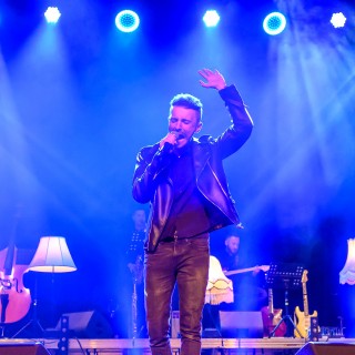 Festiwal Tarnowianie - dzień 3 - Mężczyzna stoi na scenie i śpiewa do mikrofonu z jedną uniesioną ręką.  - Fot. Przemysław Sroka