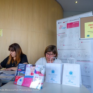 Urodziny Mościc - Kobieta siedzi na krześle przed stanowiskiem "Profilaktyka raka piersi", po drugiej stronie stolika siedzą dwie kobiety.  - Fot. Przemysław Sroka i Michał Żurowski