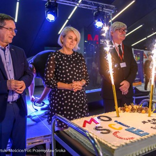 Urodziny Mościc - Kobieta w sukience oraz dwóch mężczyzn w garniturach stoją przed tortem na którym świecą się dwie świeczki.  - Fot. Przemysław Sroka i Michał Żurowski