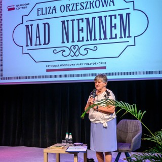 Senior w Centrum - Narodowe Czytanie - "Nad Niemnem" - Anna Krakowska stoi na scenie, trzyma w dłoni mikrofon i przemawia do słuchaczy. - Fot: Przemysław Sroka
