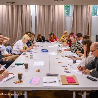 Warsztaty poetyckie Źródło - Uczestnicy warsztatów siedzą wspólnie przy stole i pracują. Przed sobą mają kartki i zdjęcia. - Fot: Przemysław Sroka