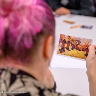 Warsztaty poetyckie Źródło - Kobieta siedzi przy stole i trzyma zdjęcie w dłoni. - Fot: Przemysław Sroka