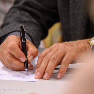 Warsztaty poetyckie Źródło - Zbliżenie na dłonie uczestknika warsztatów. Mężczyzna trzyma w dłoni pióro i pisze na kartce. - Fot: Przemysław Sroka
