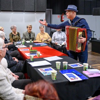 Senior w Centrum - Kolędowanie - Kobiety siedzą przy stole i śpiewają. Przed nimi stoi mężczyzna z akordeonem. - Fot: Przemysław Sroka