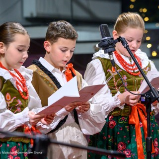Senior w Centrum - Kolędowanie - Dwie dziewczynki i chłopiec, ubrani w stroje ludowe, trzymają śpiewniki w dłoniach i śpiewają. - Fot: Przemysław Sroka